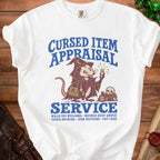 White t-shirt with blue text "Cursed Item Appraisal Service" and a possum wizard holding a ring.