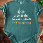 Teal t-shirt with skull, flower, and text "just trying to make friends with necromancy".