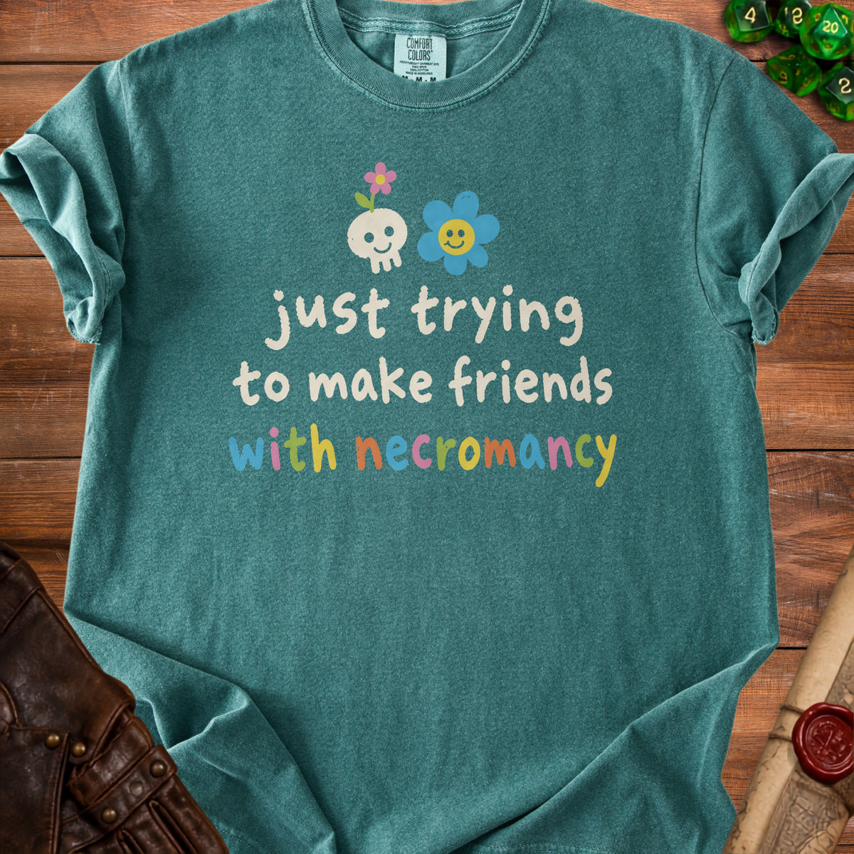 Teal t-shirt with skull, flower, and text "just trying to make friends with necromancy".