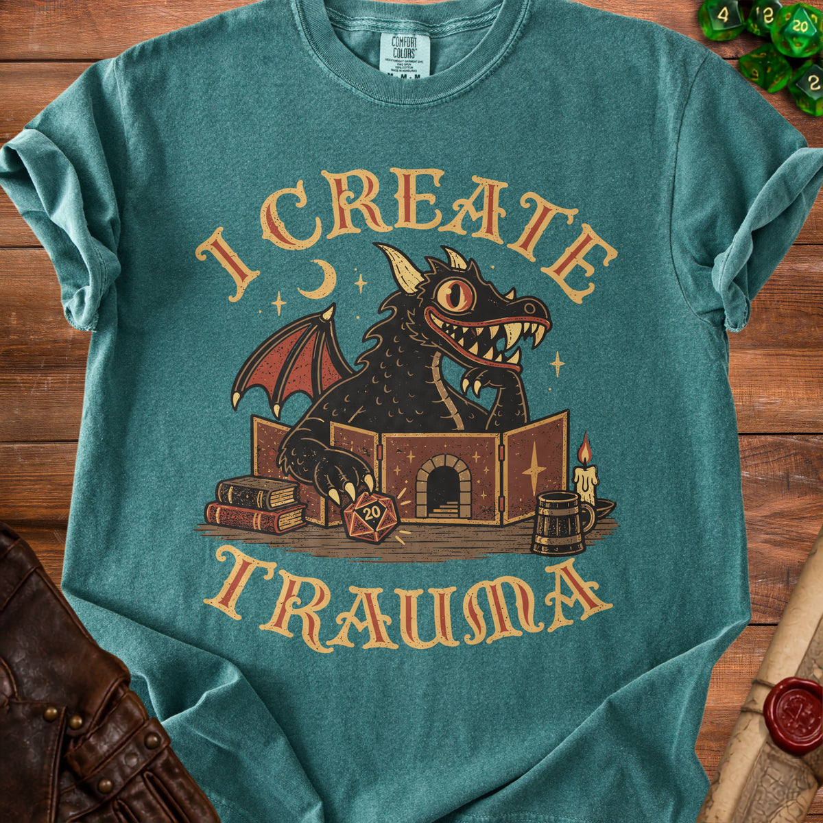A teal t-shirt featuring a cartoon dragon DM behind a screen, with text reading I CREATE TRAUMA.