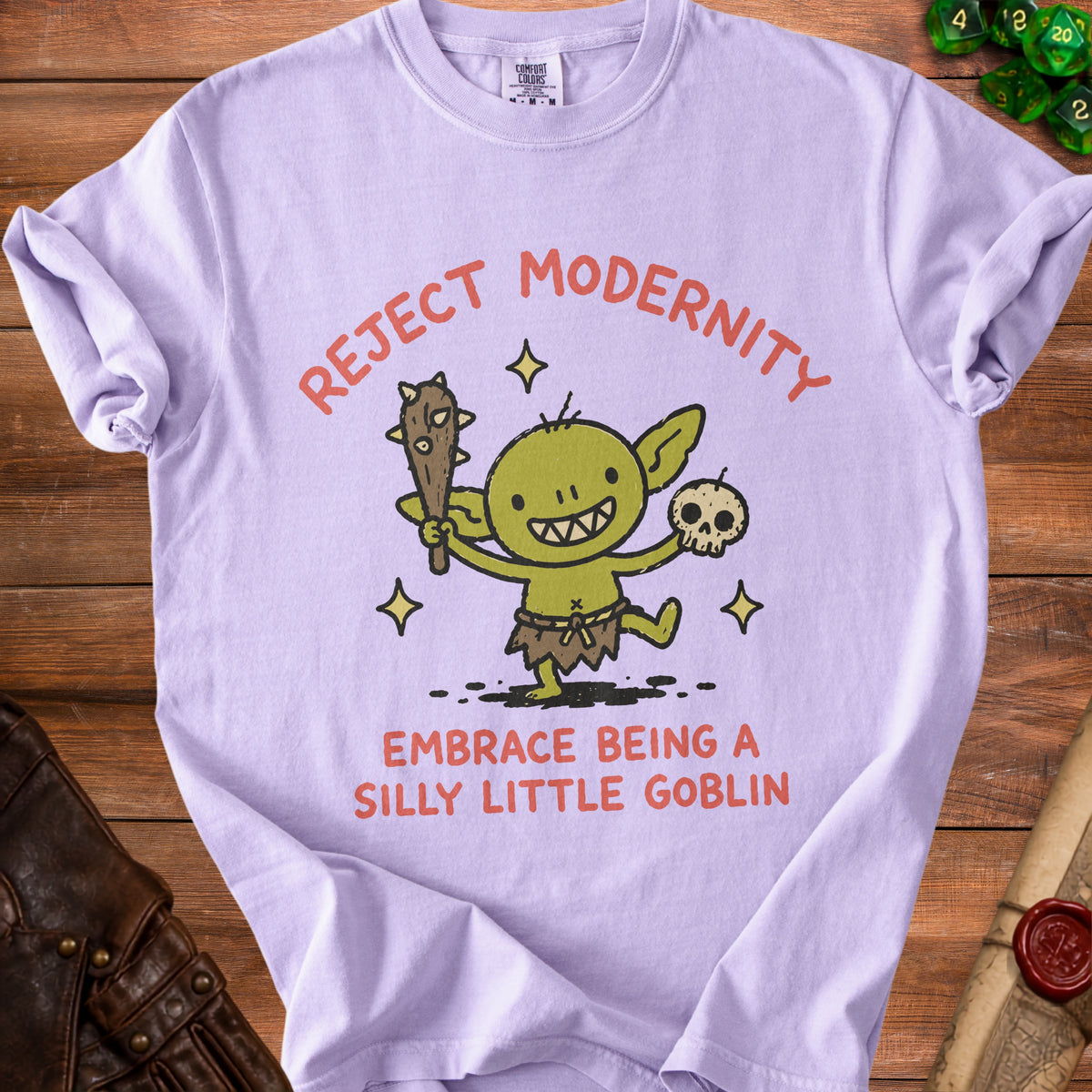 Lilac t-shirt with a cartoon goblin holding a club and skull, reading "Reject Modernity Embrace Being a Silly Little Goblin".