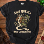 Black t-shirt with raccoon carrying a backpack and a long scroll with "SIDE QUESTS HAVE CONSEQUENCES".