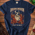 T-shirt with "Coven Before Conversation, First We Brew" text and witchy coffee graphic.