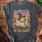 Frog in witch hat with coffee sits on lotus, text says "emotionally IN THE SWAMP."