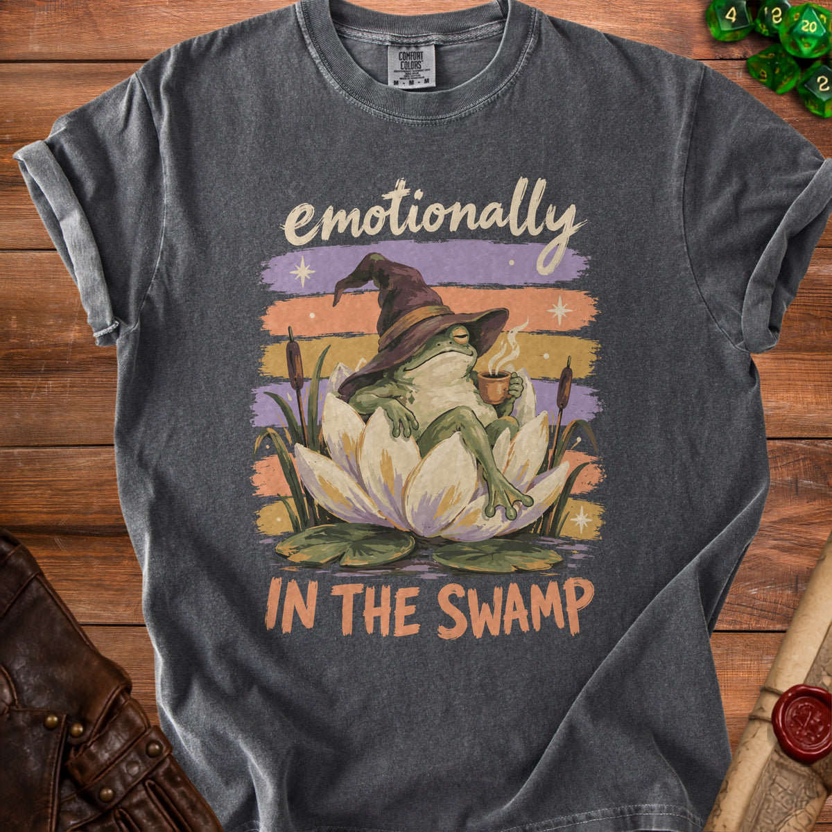 Frog in witch hat with coffee sits on lotus, text says "emotionally IN THE SWAMP."