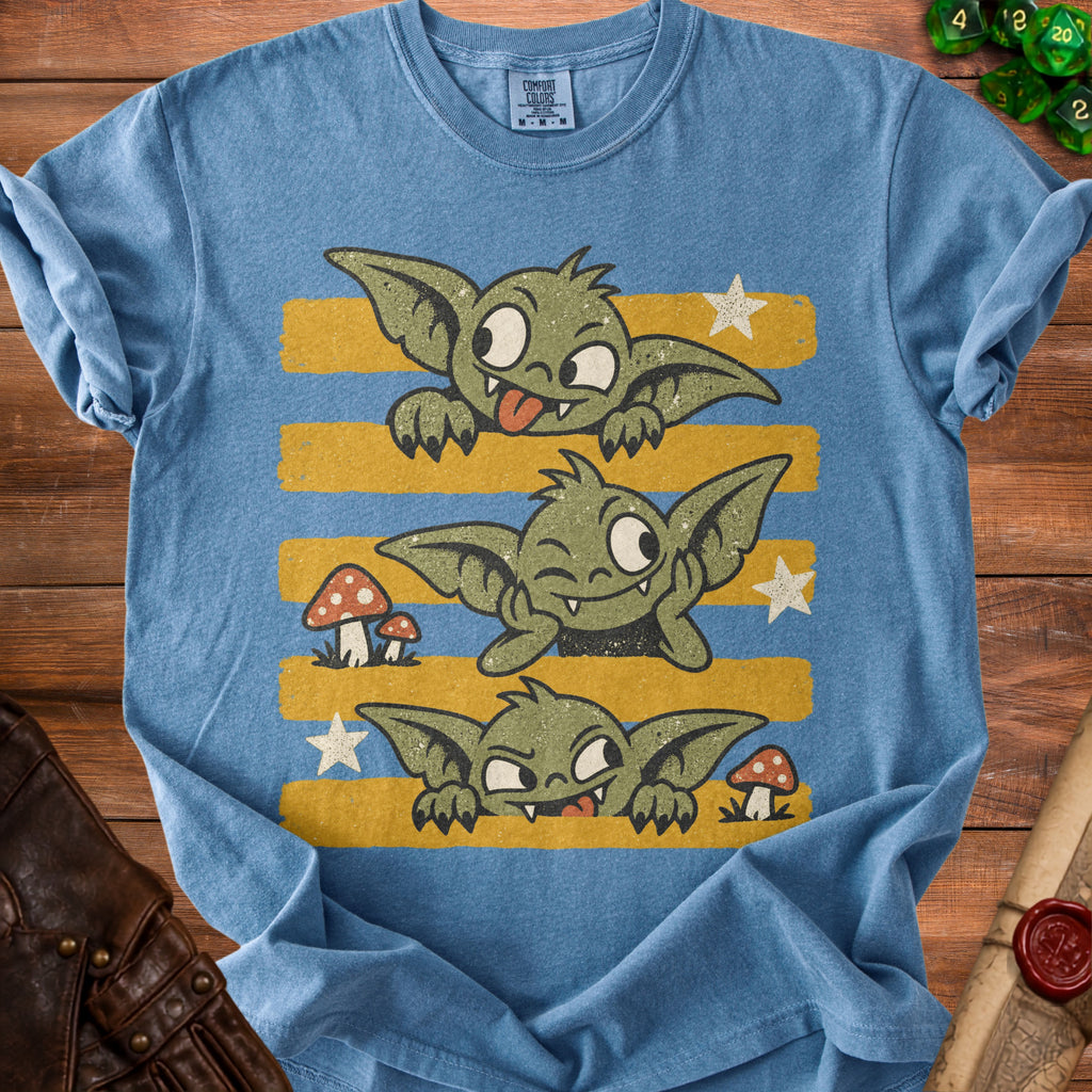 Blue t-shirt with three green goblins on yellow and blue striped background.
