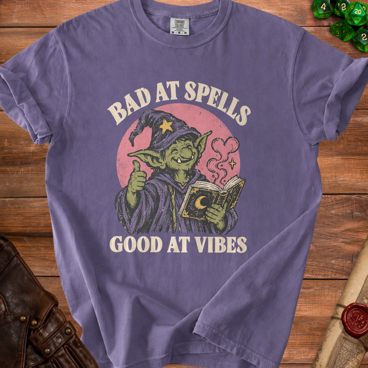 Purple t-shirt with goblin reading a book, "Bad at Spells, Good at Vibes" text.