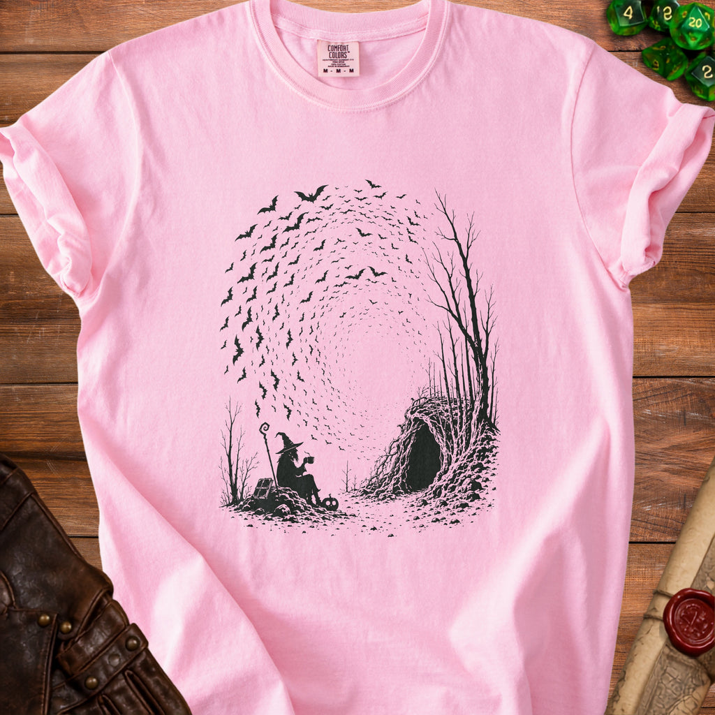 Pink t-shirt with black print of a witch, bats, and a cave entrance.