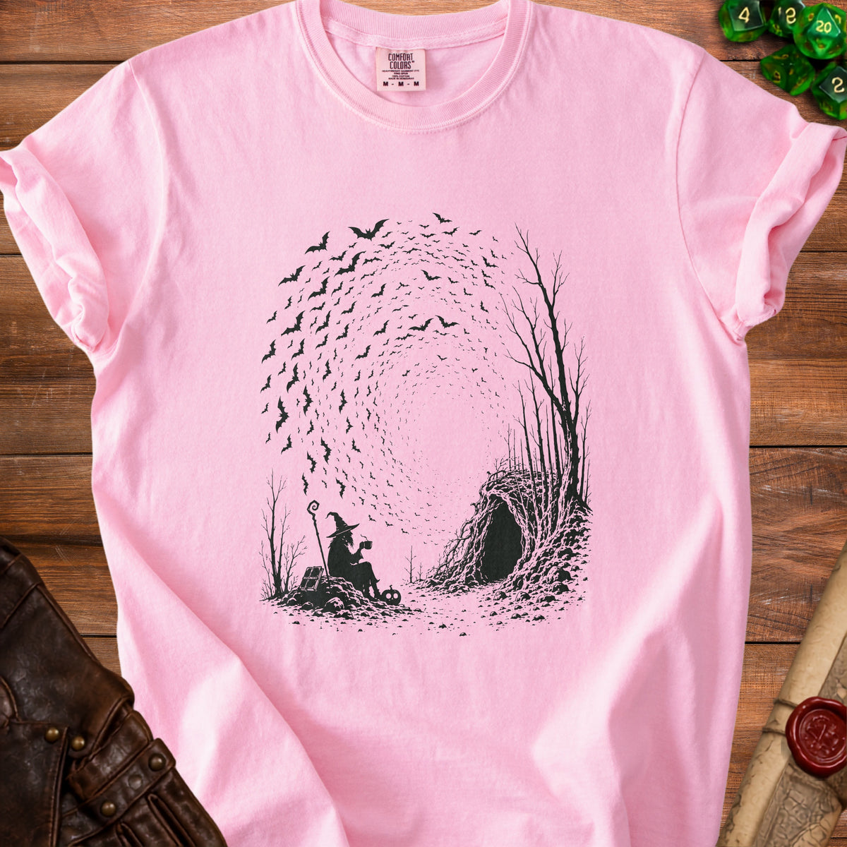 Pink t-shirt with black print of a witch, bats, and a cave entrance.