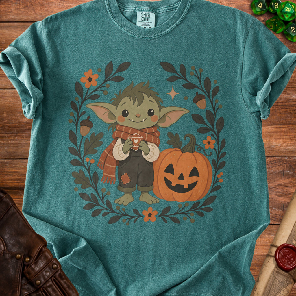 Green t-shirt with illustration of cute creature, jack-o'-lantern, and autumn leaves.