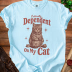 Light blue t-shirt with "Critically Dependent On My Cat" text and cat with dice.