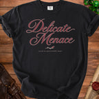 Black t-shirt with "Delicate Menace" and "raised by questionable magic" text.