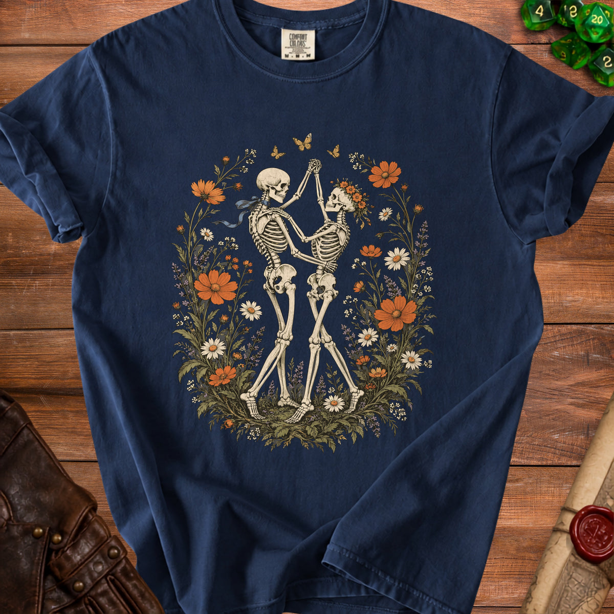 Navy blue t-shirt featuring an illustration of two skeletons dancing amidst a floral wreath.