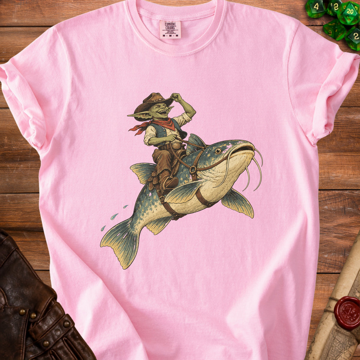 Goblin cowboy riding a catfish across a pink t-shirt.