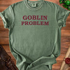 Green t-shirt with "GOBLIN PROBLEM" text, dice, and leather accessories.