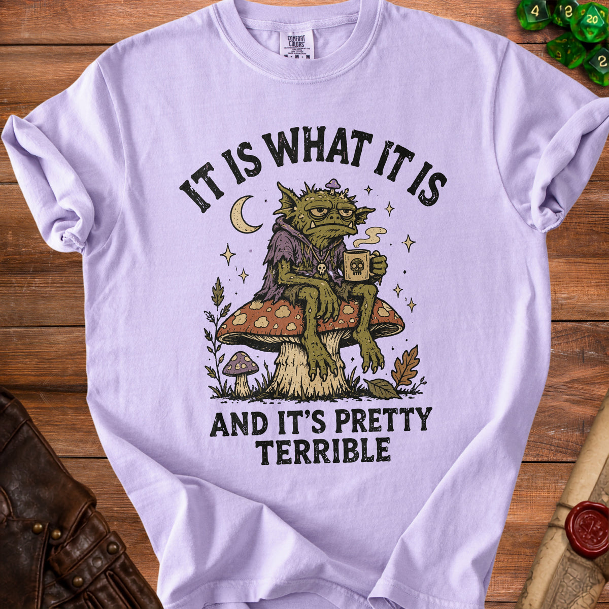 Purple t-shirt with goblin sitting on mushroom, holding coffee, text "IT IS WHAT IT IS AND IT'S PRETTY TERRIBLE."