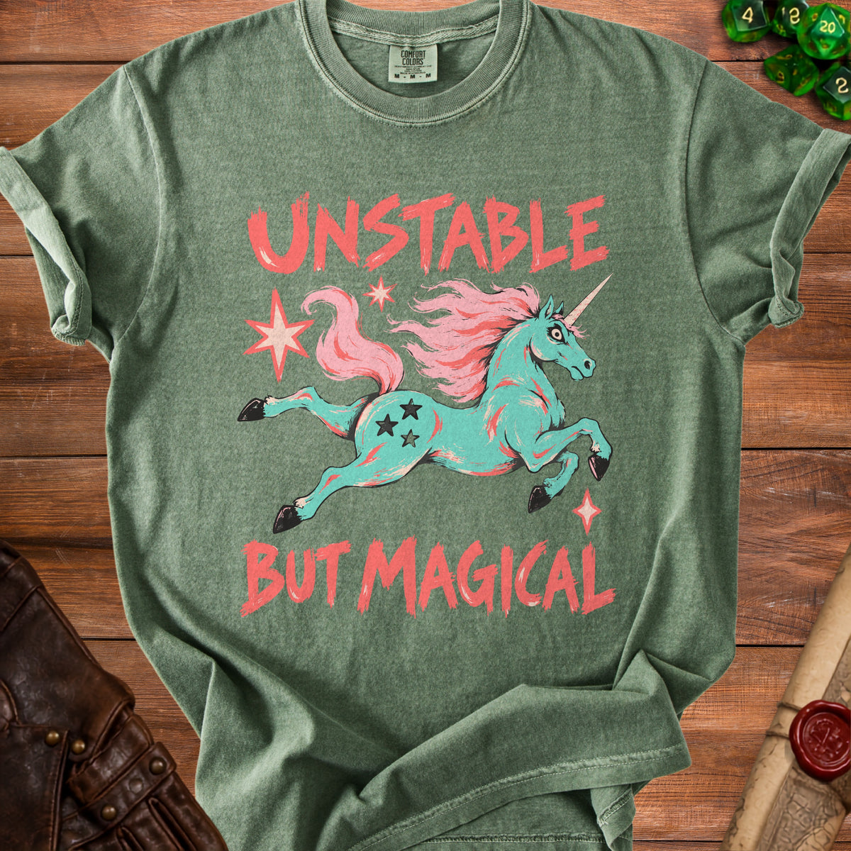 Green t-shirt with aqua unicorn graphic and coral text "UNSTABLE BUT MAGICAL".