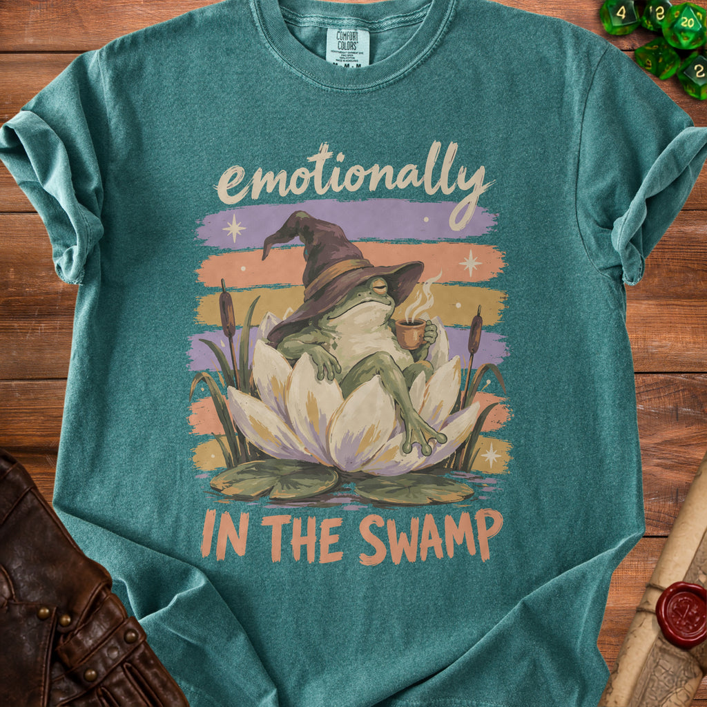 Teal t-shirt with a frog wearing a witch hat drinking coffee and text "Emotionally In The Swamp."
