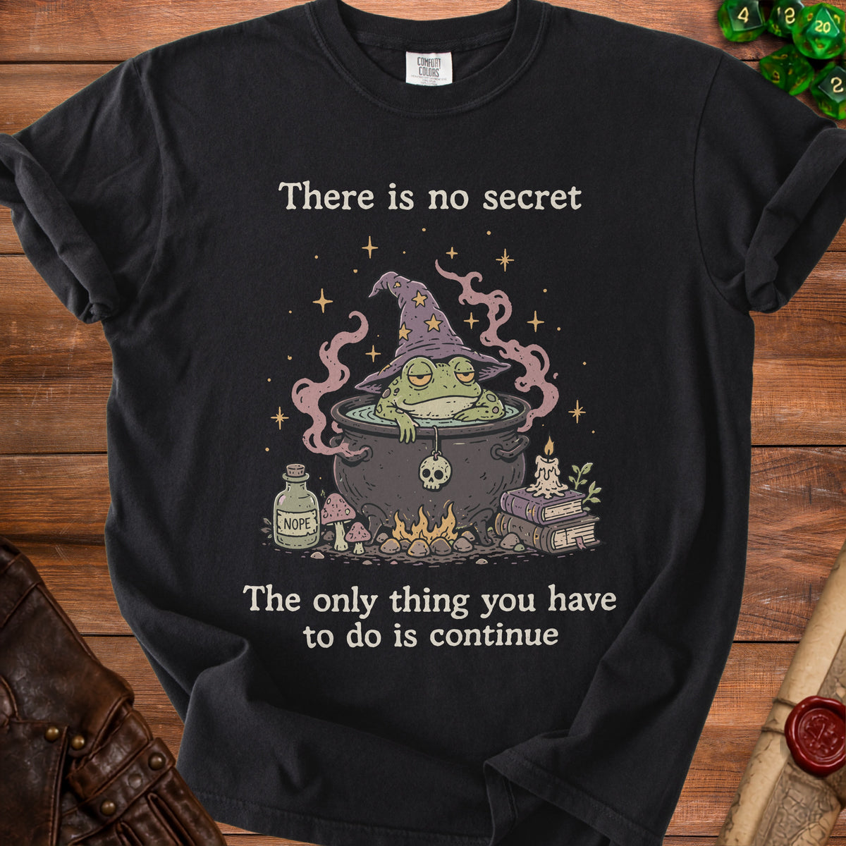 Black t-shirt with a graphic of a frog in a witch hat and cauldron, text reads "There is no secret. The only thing you have to do is continue."