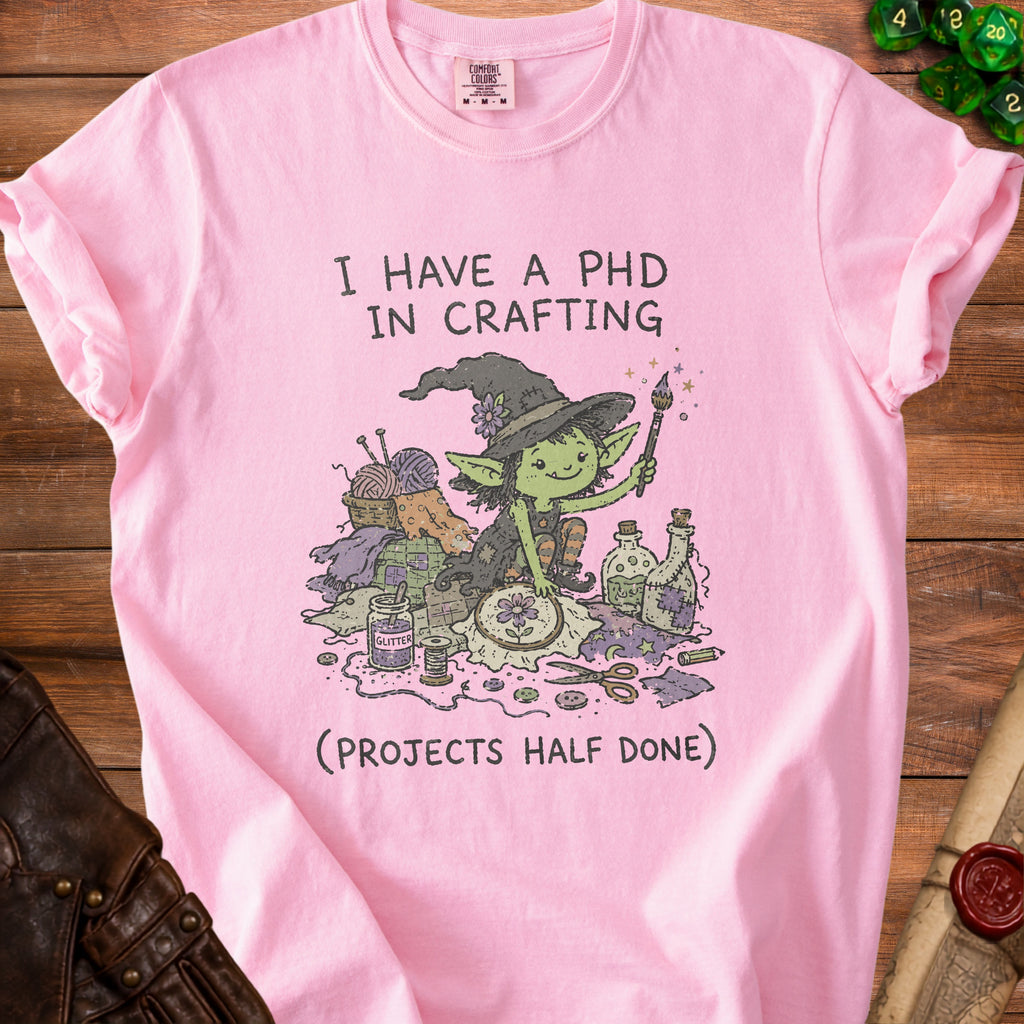 Pink t-shirt with illustration of a witch surrounded by crafting supplies and text.