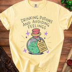 Yellow t-shirt with "Drinking Potions and Avoiding Feelings" and a potion.