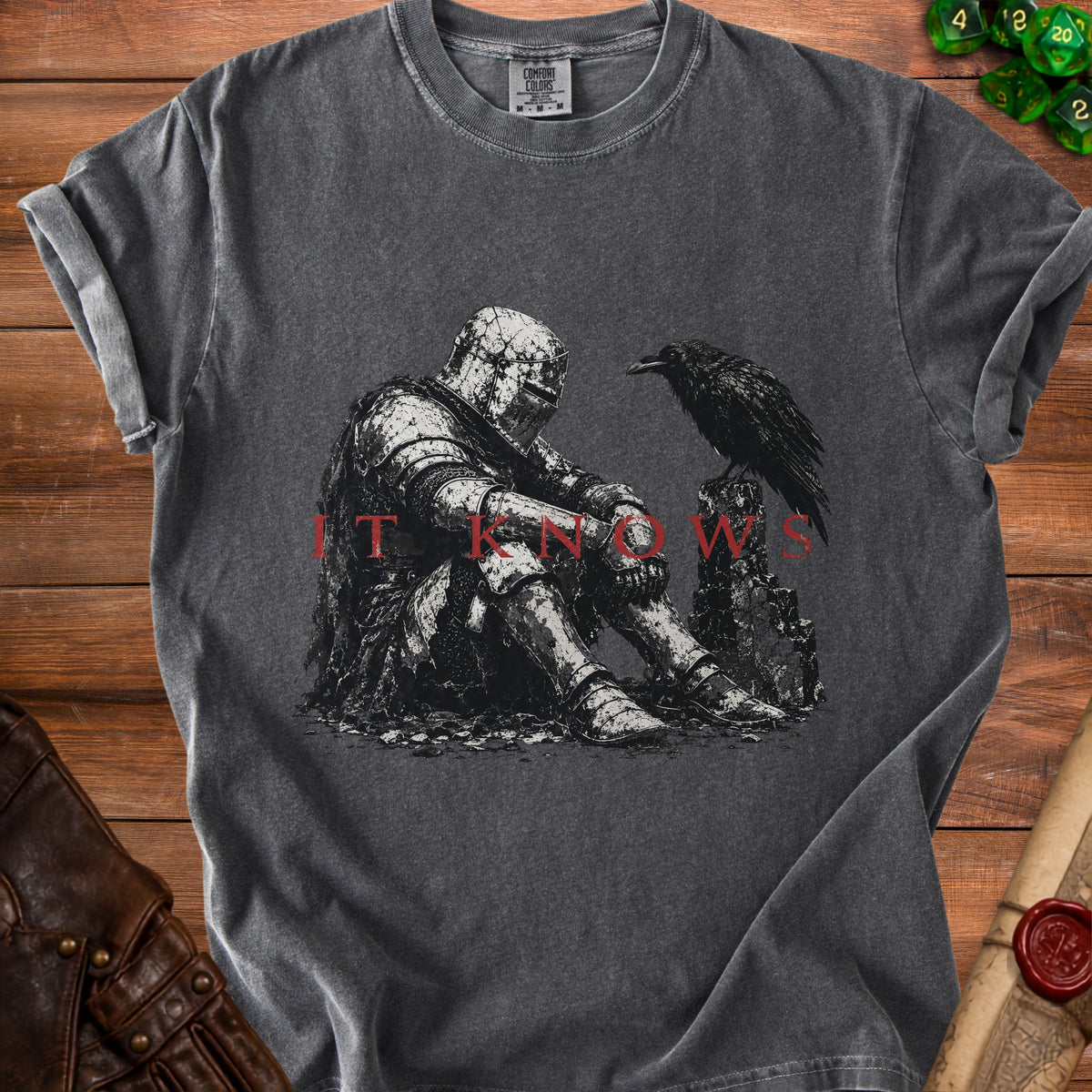 Dark t-shirt with a graphic of a knight sitting next to a raven, text "IT KNOWS".