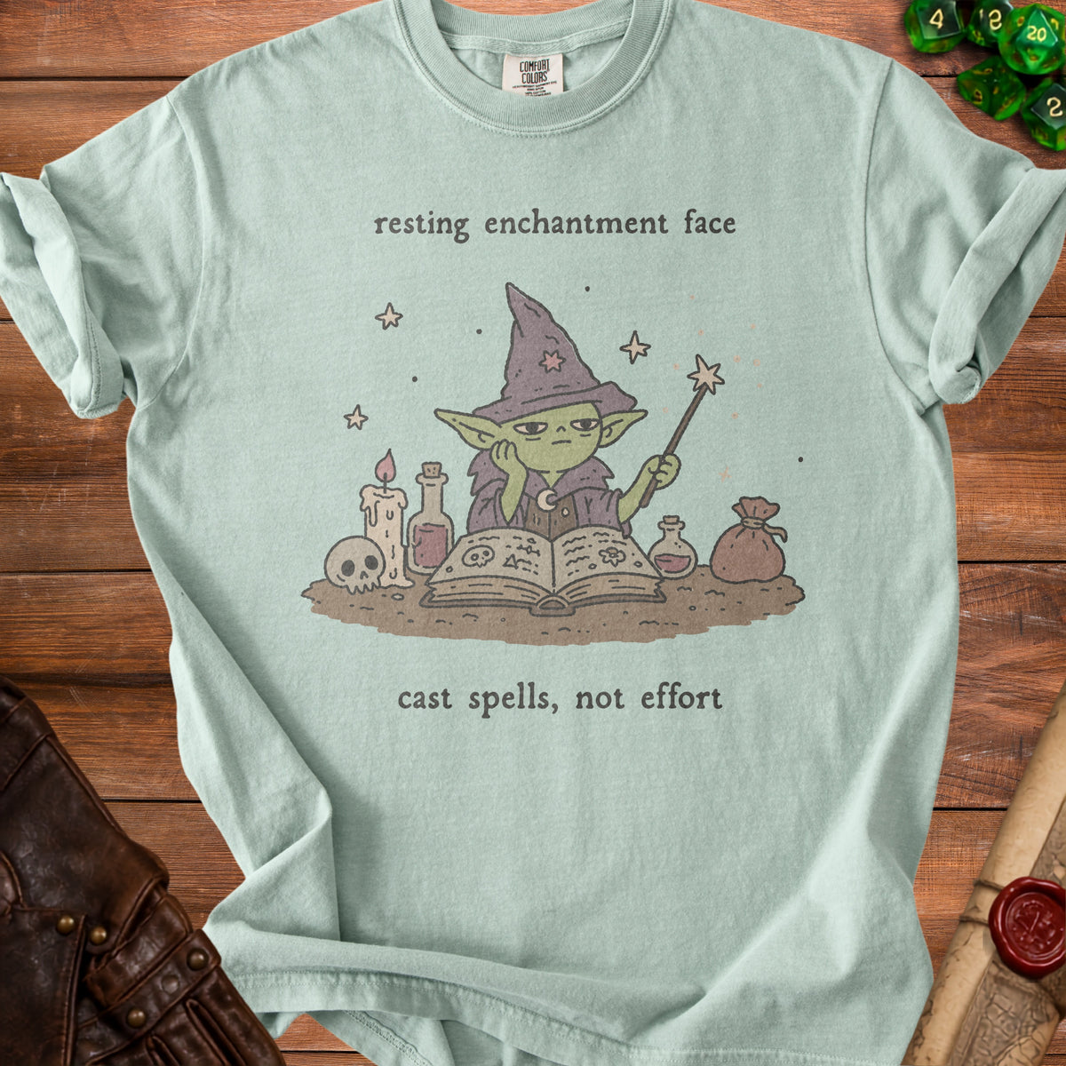Light green t-shirt with a drawing of a green wizard, a book, and potions, with text.