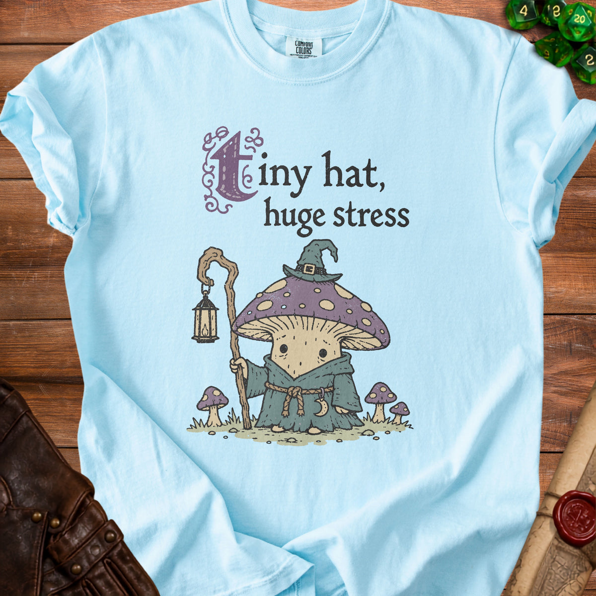 Light blue t-shirt with a mushroom wizard graphic and text "tiny hat, huge stress".