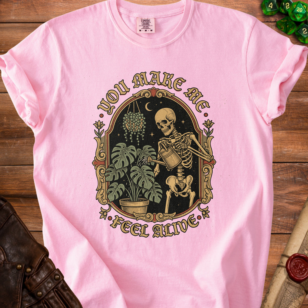 Pink t-shirt with a skeleton watering plants, text "YOU MAKE ME FEEL ALIVE".