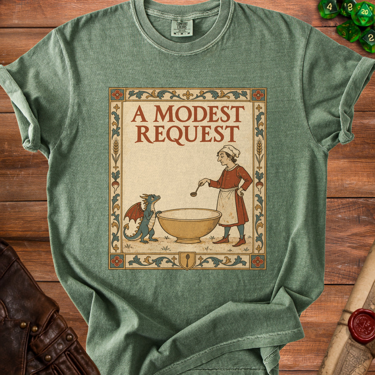Green t-shirt featuring a medieval-style illustration of a cook and dragon beside a bowl, with text "A Modest Request".