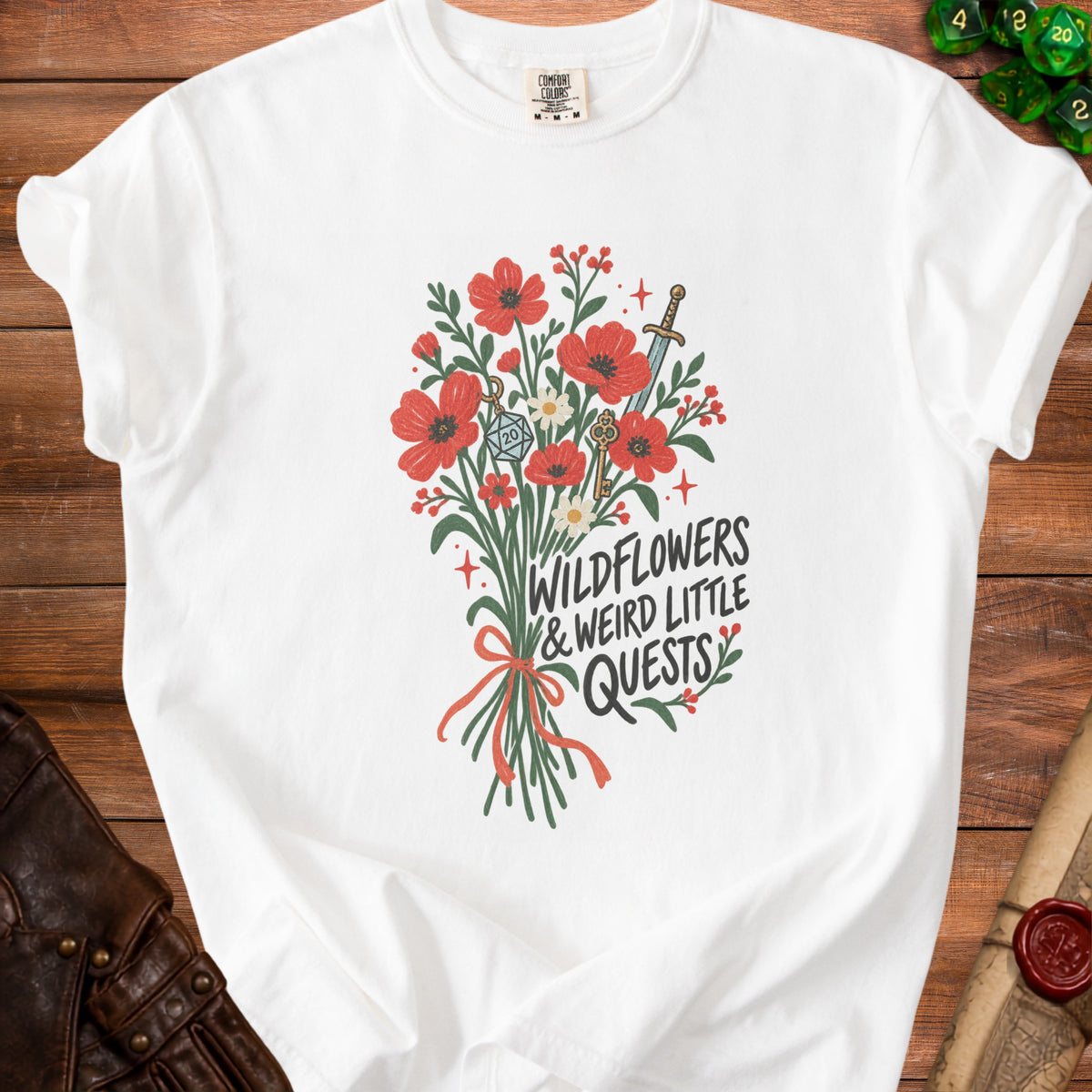 White t-shirt with red wildflowers, a sword, keys, and the text "WILDFLOWERS & WEIRD LITTLE QUESTS".