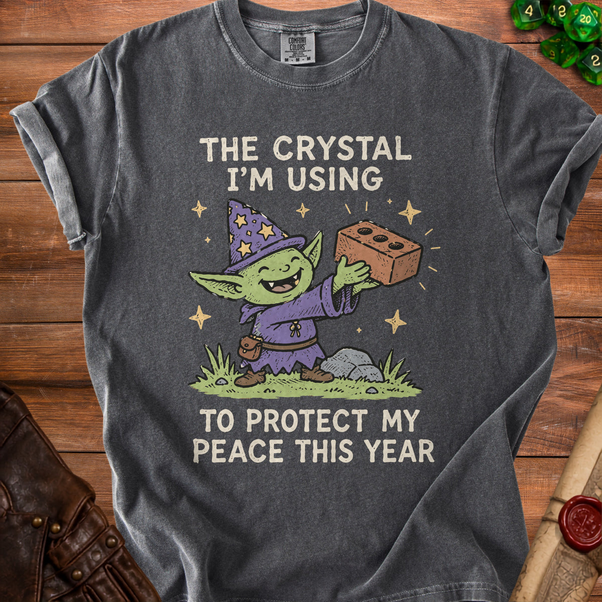 Dark gray t-shirt with cartoon goblin holding a brick and text "The crystal I'm using to protect my peace this year".