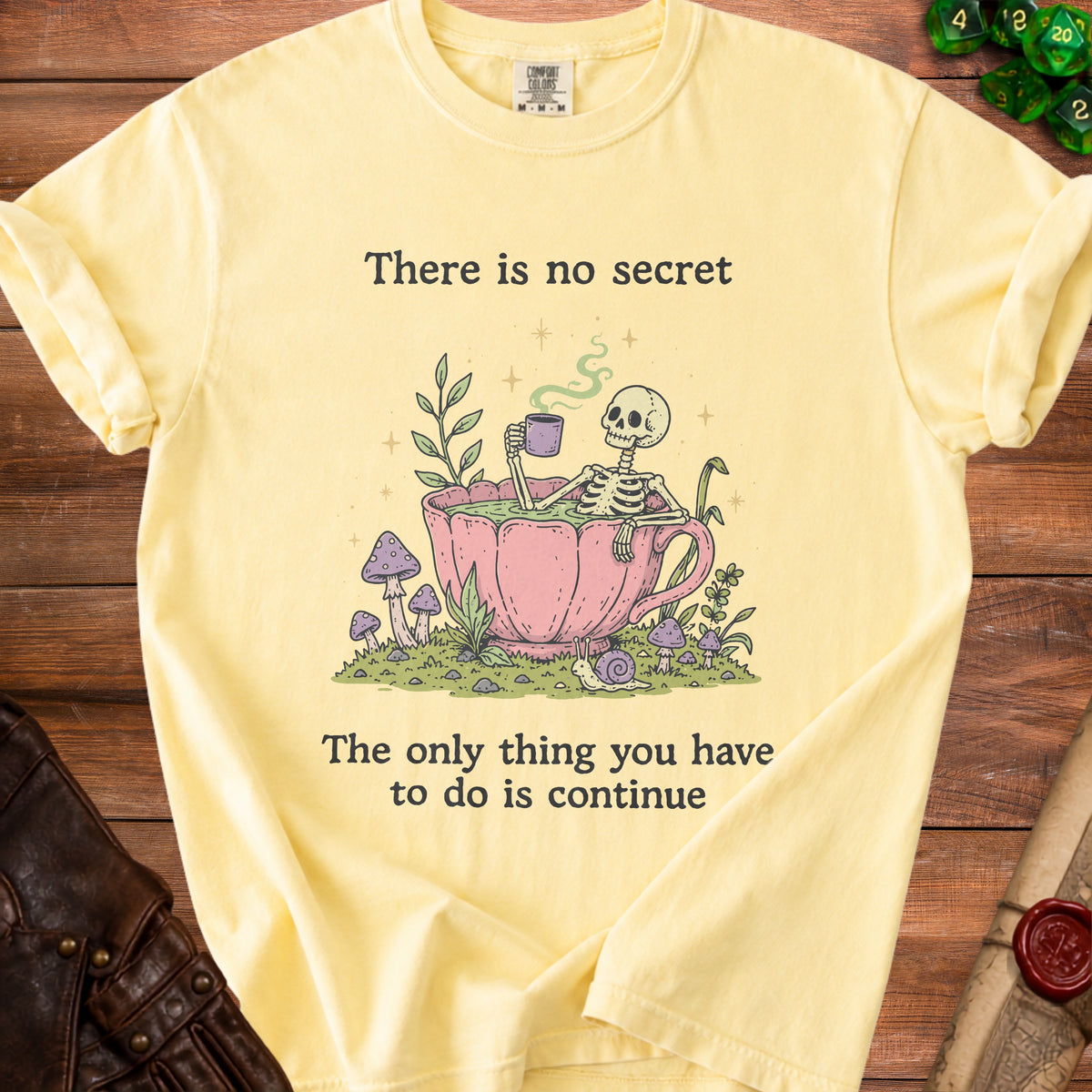 Yellow t-shirt with skeleton in teacup graphic and text: "There is no secret. The only thing you have to do is continue."