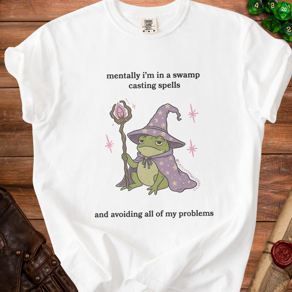 White t-shirt with frog wizard graphic and text: "mentally i'm in a swamp casting spells and avoiding all of my problems".