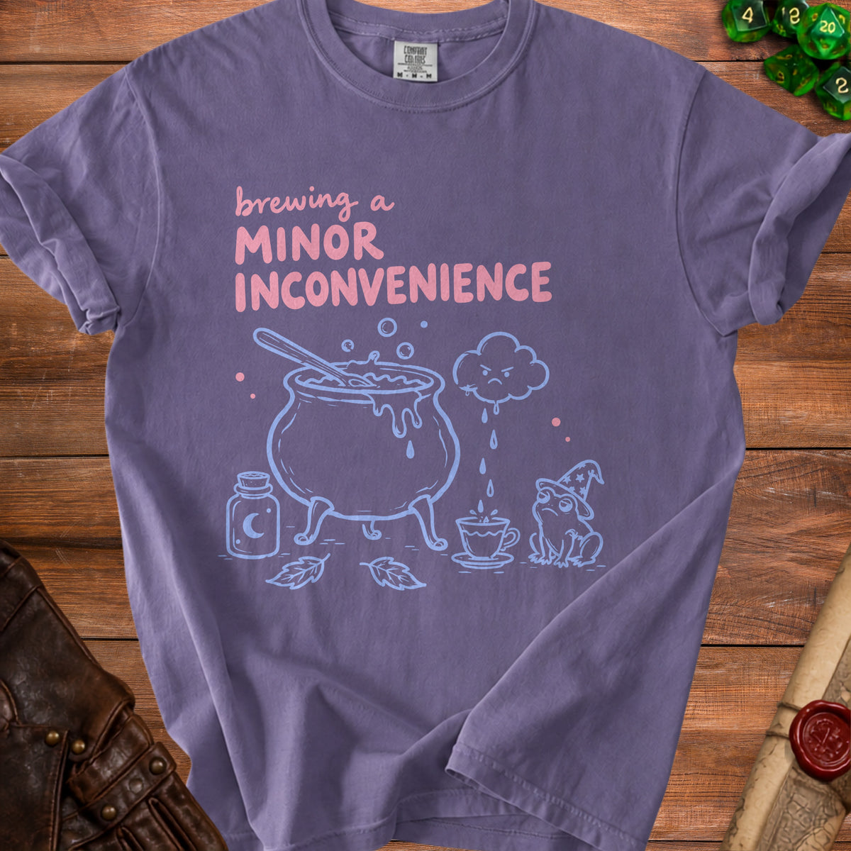 Purple t-shirt with "Brewing a Minor Inconvenience" text and witchy cauldron illustration.