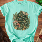 Teal t-shirt with a dark green twenty-sided die surrounded by ferns, mushrooms, and moths.