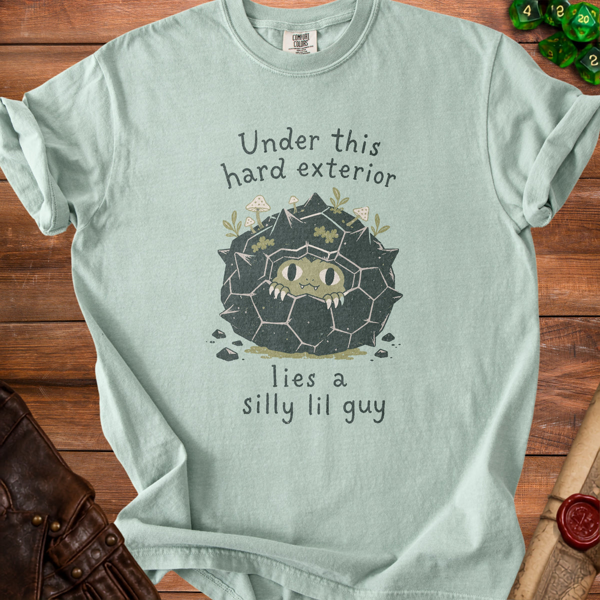 Light mint t-shirt with a creature peeking from a spiky rock and text "Under this hard exterior lies a silly lil guy".