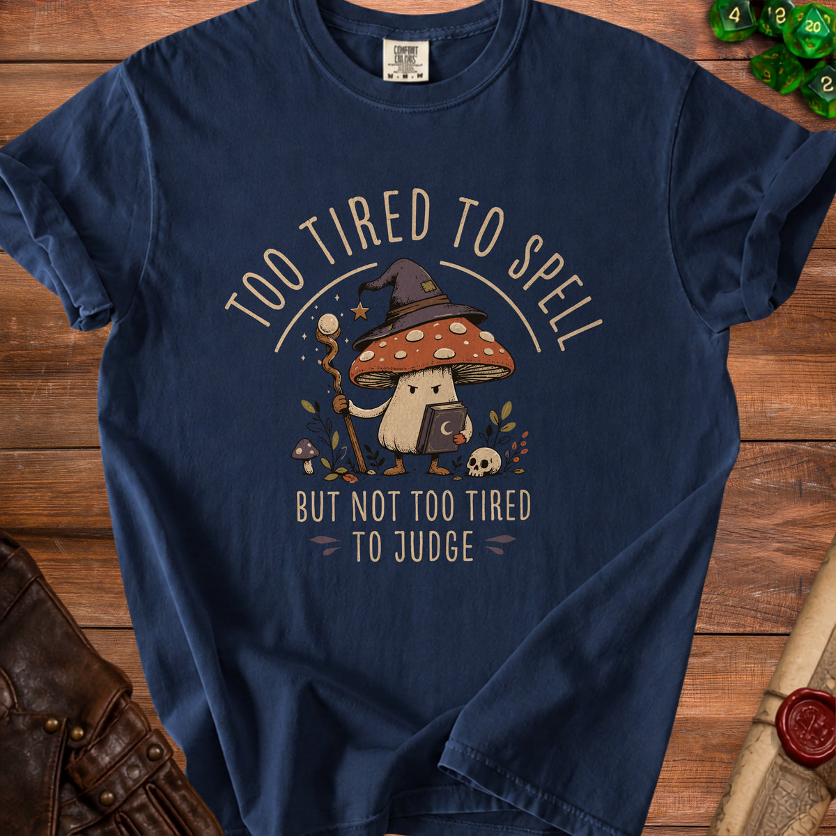 Navy t-shirt with a mushroom wizard graphic reading "Too tired to spell but not too tired to judge."