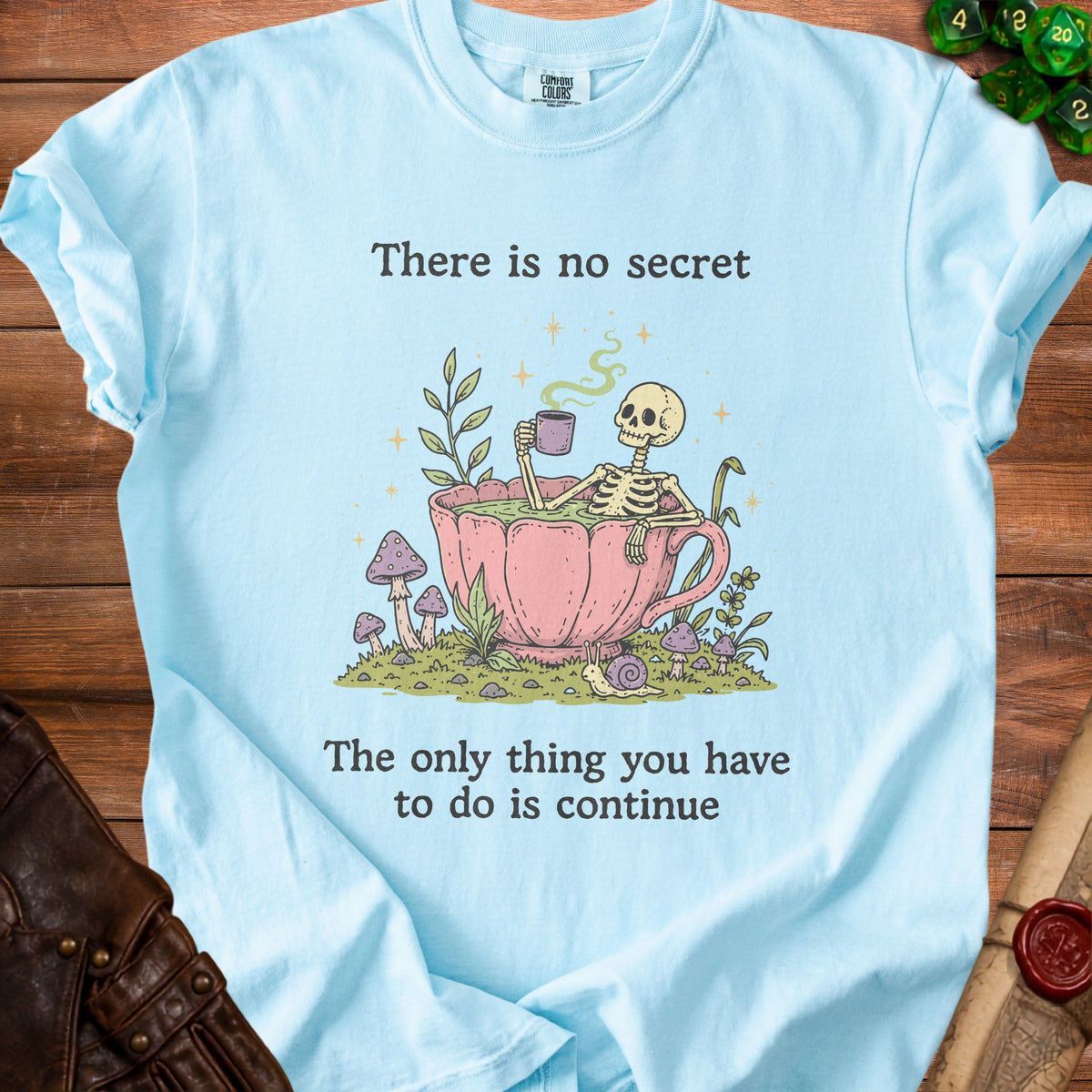 Light blue t-shirt with skeleton in teacup graphic and text: "There is no secret. The only thing you have to do is continue."