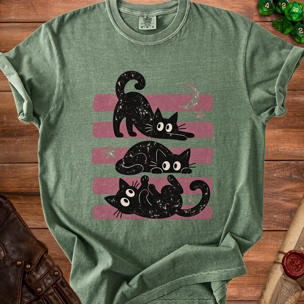 Three playful black cats with starry details on a green t-shirt with pink stripes.