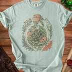 Light blue t-shirt with graphic of d20 dice inside a bottle with mushrooms and plants.