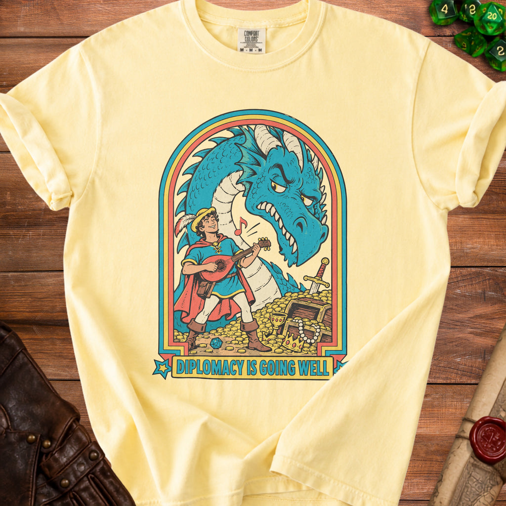 Yellow t-shirt with blue dragon, lute-playing knight, and treasure chest graphic. Text: "Diplomacy is going well."