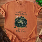 Orange t-shirt with a graphic of a rock monster and text: "Under this hard exterior lies a silly lil guy."