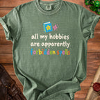 Green t-shirt with text "all my hobbies are apparently forbidden spells".