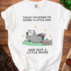 White t-shirt with a cartoon opossum and text "Today I'm going to worry a little less and nap a little more."
