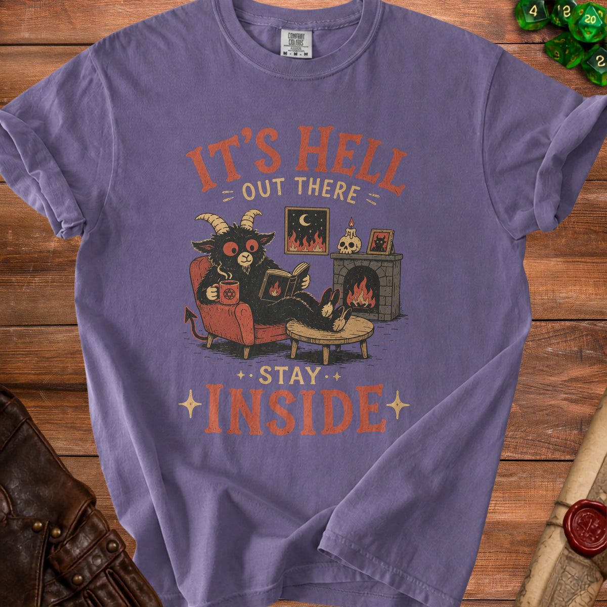 Purple t-shirt graphic: demon reading by fireplace, "It's Hell Out There, Stay Inside".