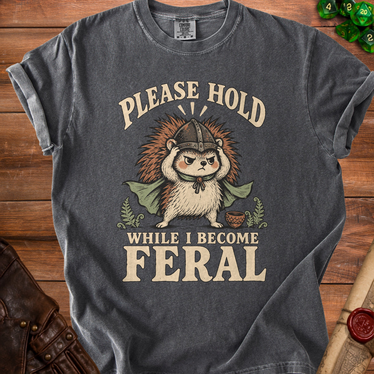 Gray t-shirt with illustration of a hedgehog in armor and text "PLEASE HOLD WHILE I BECOME FERAL".