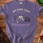 Purple t-shirt with graphic of a grumpy goat in overalls holding a shovel, text reads "MY AURA FARM WAS SHUT DOWN BY THE GOVERNMENT".