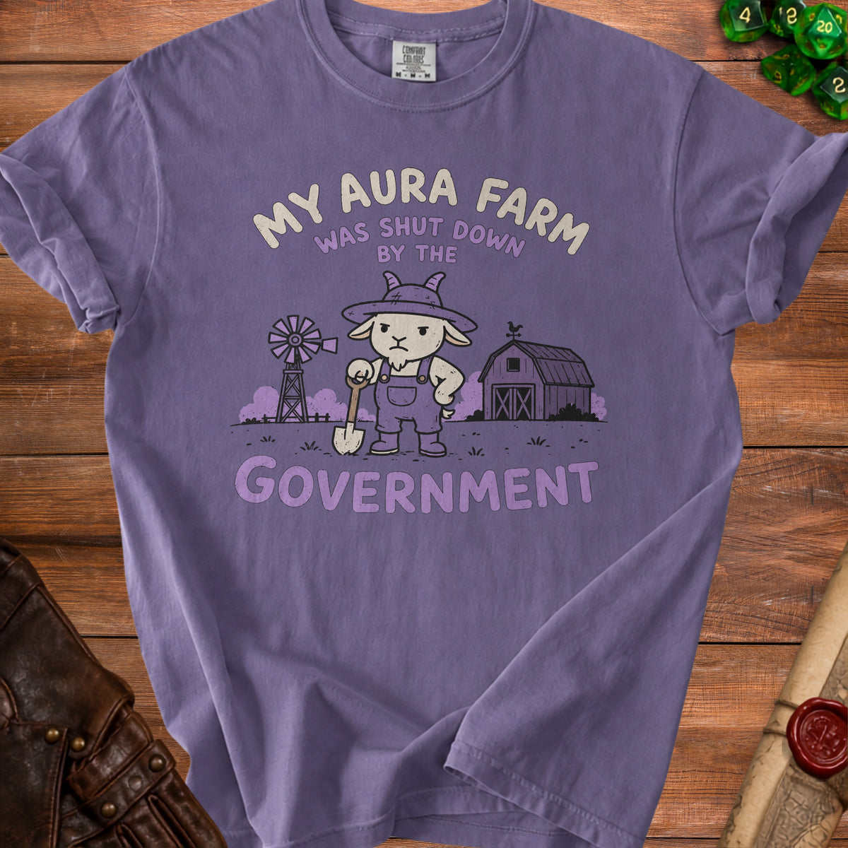 Purple t-shirt with graphic of a grumpy goat in overalls holding a shovel, text reads "MY AURA FARM WAS SHUT DOWN BY THE GOVERNMENT".