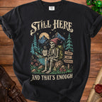 Black t-shirt with a skeleton hiking graphic and text: Still Here, Tired But Magical, and That's Enough.